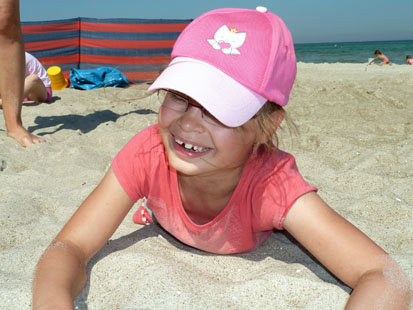 Mädchen mit rosa Dachmütze liegt im Sand und lacht