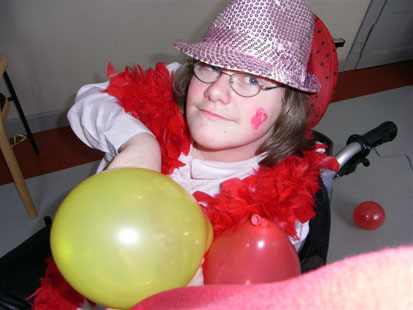 Ein Mädchen mit rotem Federschal und lila Hut spielt mit bunten Luftballons.