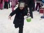 Ein Kind rennt mit einem mit Schnee gefülltem Eimer über die Schneewiese.