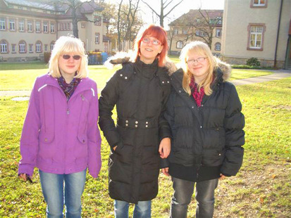 Drei fröhliche Mädchen in Winterjacken vor dem Haus.