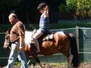 Ein Mann führt ein Pony. Darauf reitet ein Mädchen freihändig.