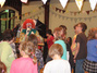 Ein Clown spricht in ein Mikrofon, die Kinder hören gespannt zu.