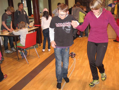 Ein Junge balanciert auf einem Seil, eine junge Frau hilft ihm dabei.