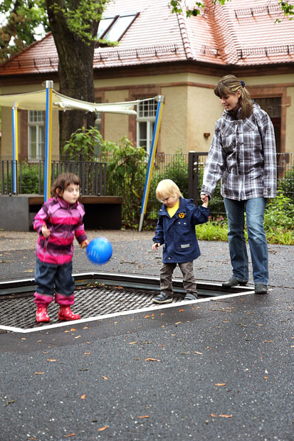 Erzieherin betreut zwei Kinder auf dem Trampolin 