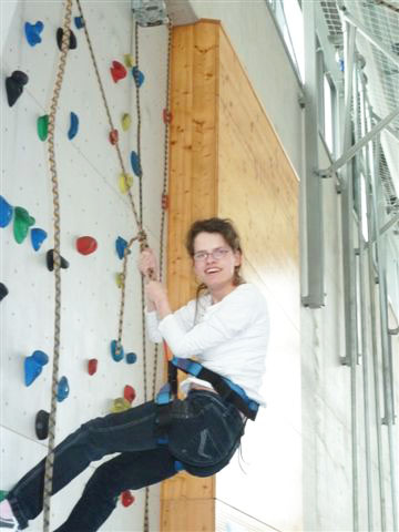 Mädchen hängt am Seil oben vor der Kletterwand