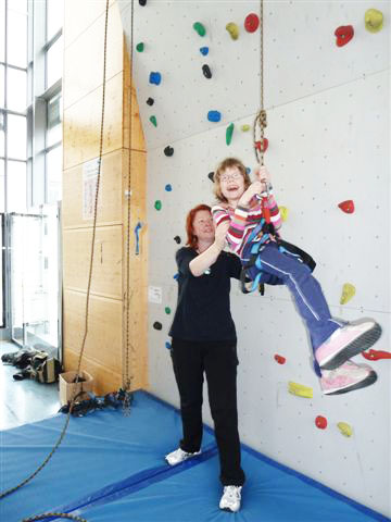 Erzieherin steht vor der Kletterwand und hilft einem Mädchen