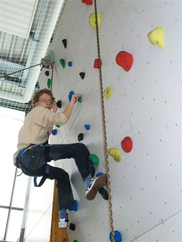 Junge oben an der Kletterwand, gesichtert mir Kletterausrüstung