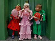 Drei Kinder in Faschingskostümen und Luftballons.