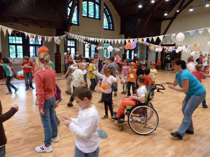 Viele Kinder und Betreuerinnen tanzen in einem großen, bunt geschmückten Saal
