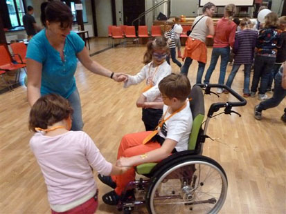 Kind im Rollstuhl tanzt mit zwei anderen Kindern und einer Betreuerin